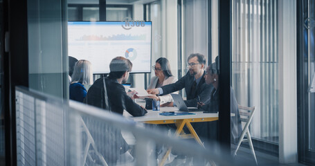 Fototapeta na wymiar Business Team Meets in a Glass Conference Room to Review Financial Dashboards, Share Printed Reports, Discuss Performance Trends, and Agree on Strategy, Using Laptops, Charts, and Digital Tools