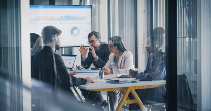 Business Team Meets in a Glass Office to Review Dashboards, Compare Sales Results, and Plan Strategy, Using Laptops, Charts, and Reports to Align Goals, Refine Budgets, Coordinate Upcoming Project