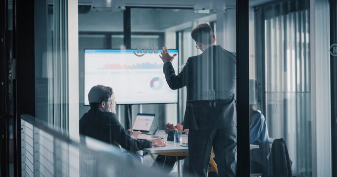 Business Team Meets in a Glass Conference Room to Review Digital Dashboards, Discuss Sales Performance, Refine Strategy, and Coordinate Upcoming Projects, Using Laptops, Charts