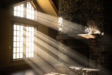 Obraz premium A rustic interior with a stone fireplace and large windows, bathed in golden light.