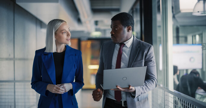 Coworkers Walk Through a Modern Office Discussing Performance Dashboards on a Laptop, Reviewing Sales Results, Aligning Priorities, Planning Next Steps, and Coordinating Cross-team Actions