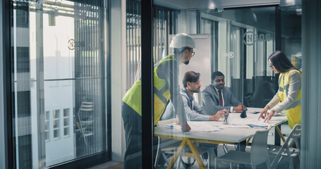 Executives and Engineers Meet in a Glass Conference Room to Review Construction Plans, Digital Dashboards, and Financial Data, Coordinating Project Scope, Schedule, Budget, Risk Management © Gorodenkoff