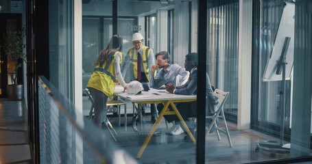Project Managers and Engineers Meet in a Glass Office to Review Construction Drawings, Plan Site Work, Align Budget and Schedule, Assess Safety and Risk, and Coordinate Communication for Business © Gorodenkoff