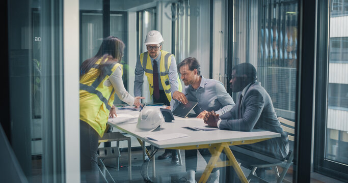 Executives and Construction Consultants Meet in a Glass Office to Review Blueprints, Align Budgets, Set Milestones, and Plan Risk, Compliance, and Stakeholder Communication Strategies for Business