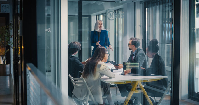 Business Executive Leads a Focused Strategy Meeting in a Glass Conference Room, Guiding Colleagues as They Review Analytics Dashboards, Define Priorities, Align Product Roadmaps, Assign Owners