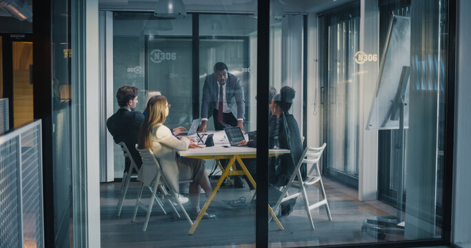 Business Manager Leads a Focused Meeting in a Glass Conference Room, Guiding Colleagues as They Review Performance Dashboards, Clarify Priorities, Align Project Milestones, Assign Responsibilities