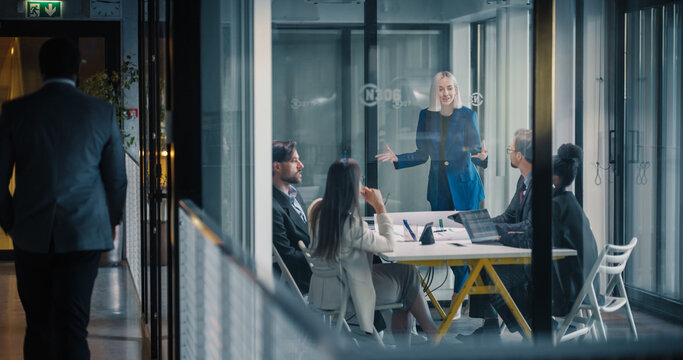 Businesswoman Leads a Strategic Planning Meeting in a Glass Conference Room, Explaining Goals, Reviewing Performance Metrics, Coordinating Tasks, and Encouraging Collaboration as Colleagues Listen