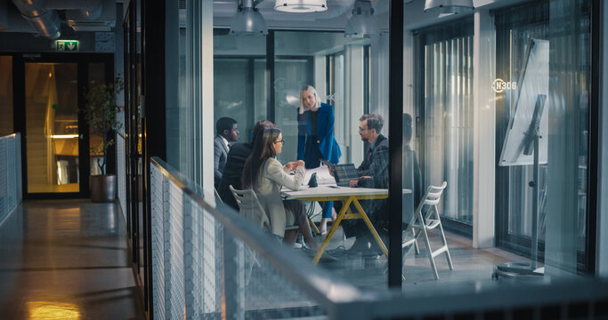 Business Team Holds a Focused Strategy Meeting in a Glass Office, as a Female Leader Guides Discussion, Reviews Digital Reports, Aligns Goals, Assigns Tasks, and Plans Next Steps for Projects