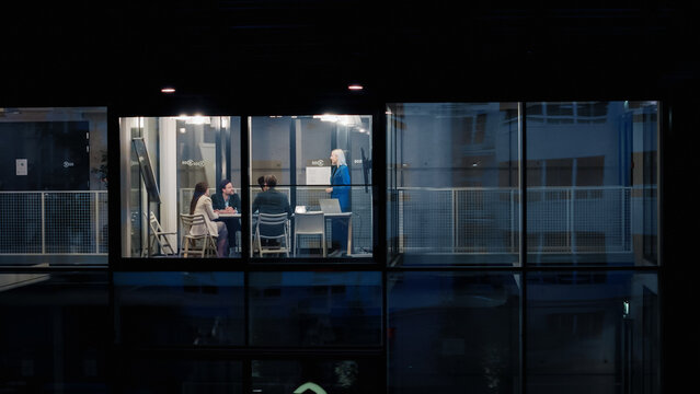 Night Office Meeting Shows a Female Manager Leading Three Coworkers Through a Clear Strategy Review, Using a Laptop, Charts, and Notes to Set Goals, Refine Plans, and Coordinate Upcoming Projects