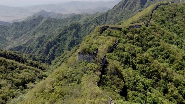 Wild Great Wall ruins along mountain ridge with overgrown watchtower and dramatic landscape, China