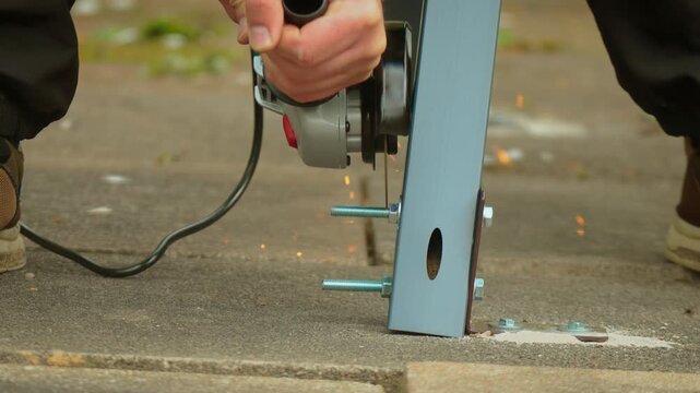 Angle grinder cutting protruding metal bolt on steel bracket mounted to concrete surface close up. Sparks flying from rotating disc while trimming fastener during construction installation