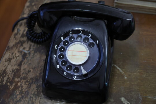A vintage black rotary dial telephone on a wooden table.