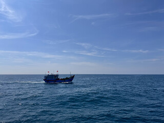 Obraz premium Lone fishing boat moving across the vast blue waters of the ocean