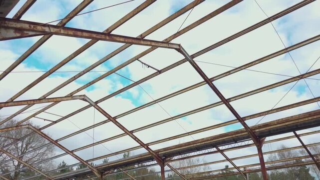 Climate impact concept with corroded metal roof structure exposed to open sky and changing weather. Upward perspective highlighting rust decay environmental damage and abandoned industrial framework
