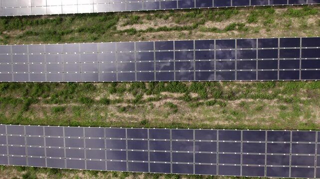 Drone flying over a solar farm with sun and clouds reflecting
