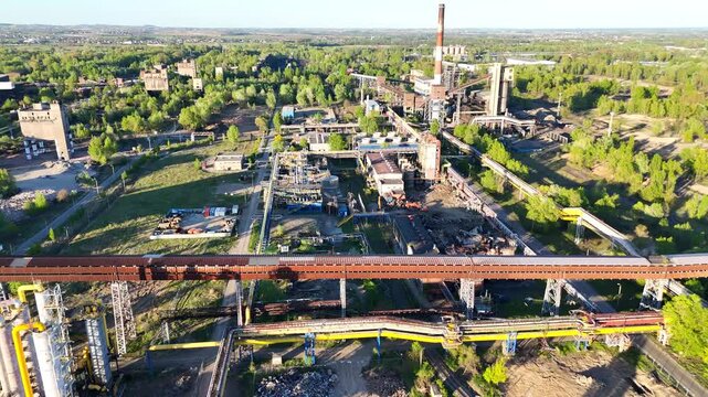 Aerial view of industrial complex with green trees and machinery, showcasing production facilities, pipelines, and surrounding landscape in a vibrant, sunlit environment