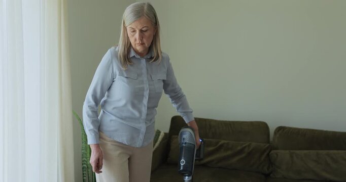 Senior woman cleaning living room at home. Older housewife feeling happy and enjoy vacuuming for housekeeping housework or chores in house.