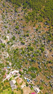 Vertical video. Kayakoy, Turkey. Aerial drone view of the abandoned ghost town ruins and stone houses on mountain slopes under clear blue sky and bright sunlight.. Aerial View, Point of interest. Ric