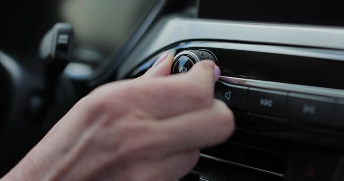 Close-up of hands turning volume button of car radio. Woman driving car. Listen to music while driving.
