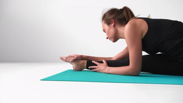 Flexible woman performing a seated forward bend yoga pose stretching her hamstrings on a mat isolated on a white background