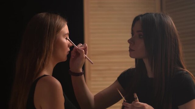 Professional makeup artist applying concealer on a model's eyelids with a brush. Slow motion shot in a beauty salon showcasing the meticulous process of eye makeup application