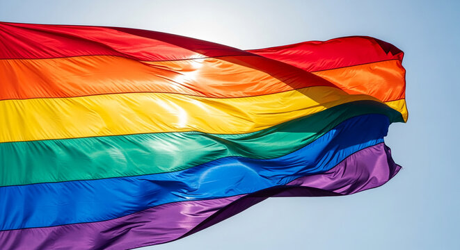 Waving rainbow flag against a clear blue sky, symbolizing pride, diversity, and equality. A vibrant representation of LGBTQ+ community and acceptance