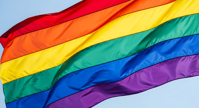Waving rainbow flag against a clear sky, symbolizing diversity, pride, and LGBTQ+ rights, a vibrant representation of equality and inclusion