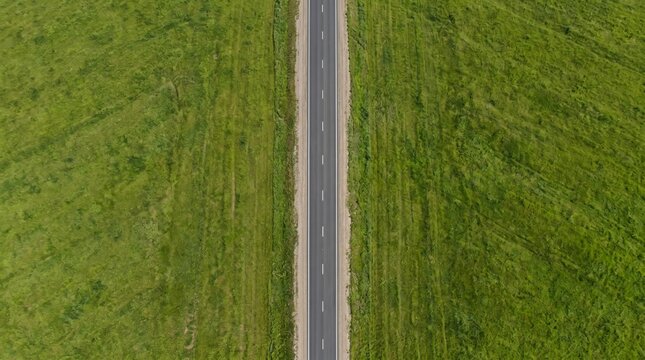 Straight asphalt road cutting through lush green grass aerial view