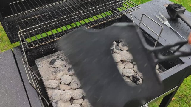 Preparing charcoal briquette grill for backyard cooking with tools and coal on a sunny day in a green garden