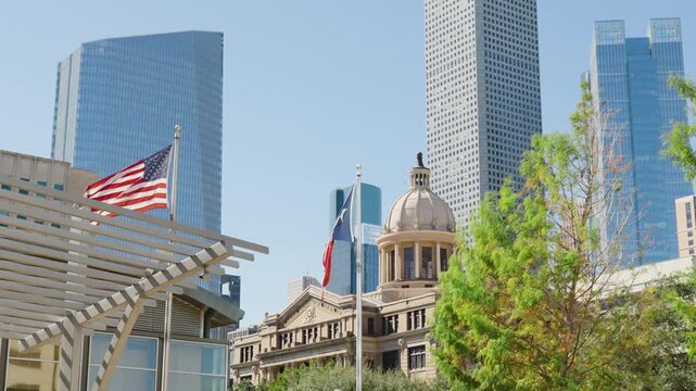 Texas and American flags waving in front of Houston City Hall with Downtown Houston skyline and modern skyscrapers in the background on a sunny day in Houston, Texas, USA.