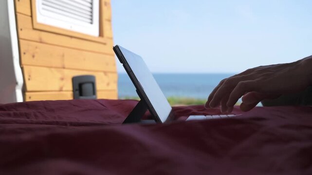 Digital nomad working on a tablet inside a camper van with the sea in the background