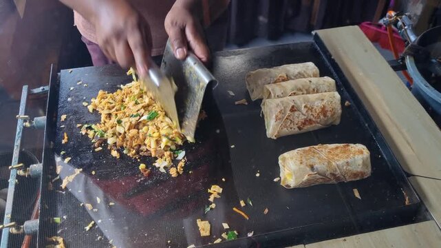 Close up of Kottu Roti cooking on a hot metal griddle in Ella, Sri Lanka, where chopped flatbread is mixed with vegetables, egg, and curry as a cook expertly chops and combines the ingredidients