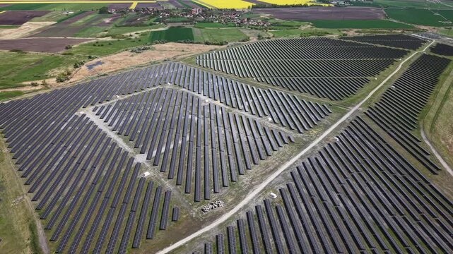 An aerial view shows a vast solar panel farm covering agricultural land, symbolizing sustainable energy infrastructure and green technology development.