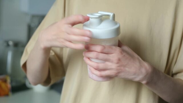 Unrecognizable woman in a kitchen closing the lid of a shaker bottle and mixing a strawberry protein shake for a healthy lifestyle, diet, and fitness nutrition to gain muscle mass