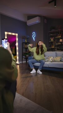 Teen girl performing hip hop dance for phone camera filmed by friend in home room social media content creator economy ugc culture