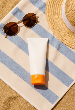 Crema solare, occhiali da sole e cappello di paglia su asciugamano da spiaggia