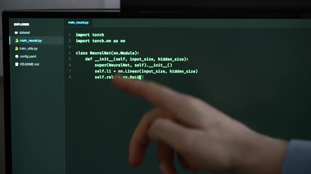 Hand pointing at programming code on computer screen.