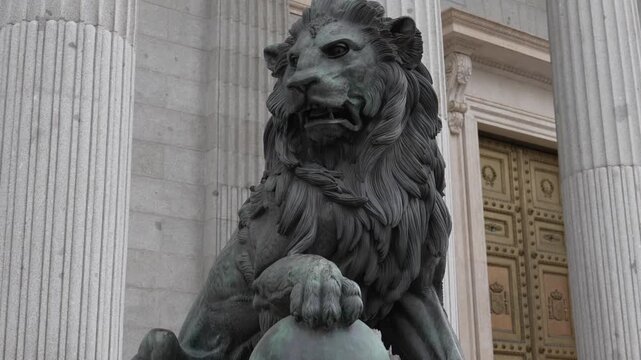 Bronze lion statue guarding the Spanish Congress in Madrid, with neoclassical columns and grand doors, symbolizing power, heritage, and national identity for travel and history themes.