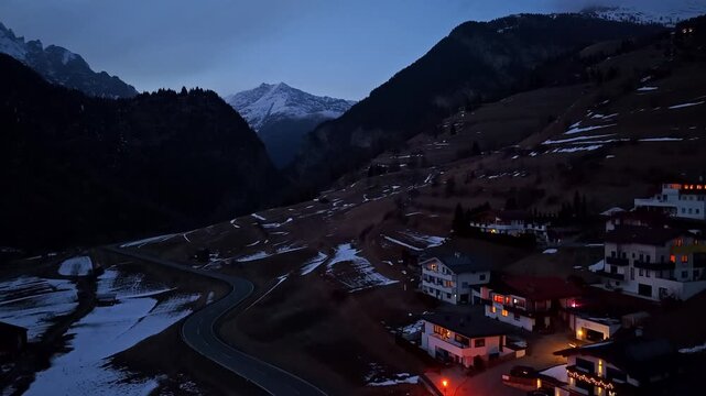 Aerial view of quiet Alpine village with illuminated buildings nestled in a dark mountain valley at dusk. Nauders, Austria