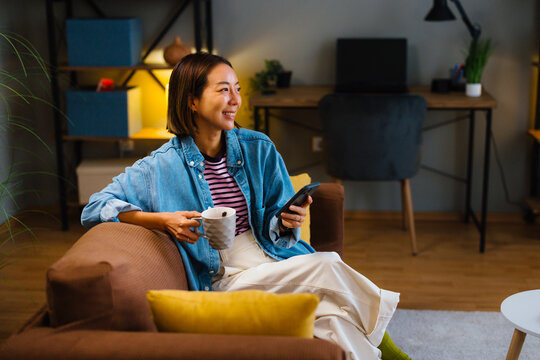 Young woman using smartphone while drinking coffee at home