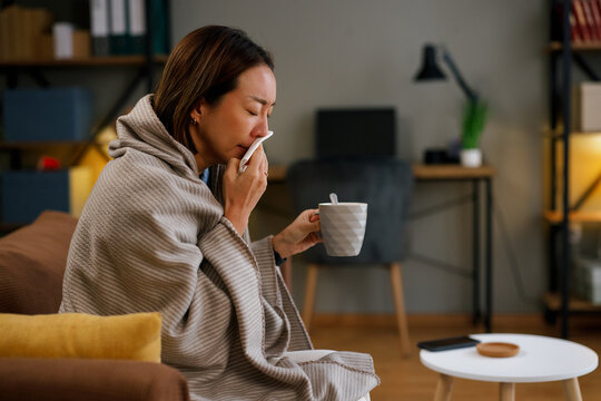 Sick woman wrapped in blanket drinking hot tea at home