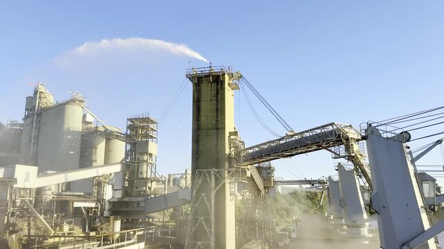 Bulk carrier loading grain at large export terminal. Grain elevators, conveyor belts and loading pipes transfer wheat to ship. Dust suppression water cascade from tower prevents grain dust pollution.
