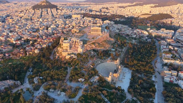 High-angle drone Video of the Parthenon atop the Acropolis hill, overlooking the vast urban sprawl of Athens and Lycabettus Hill at sunset.