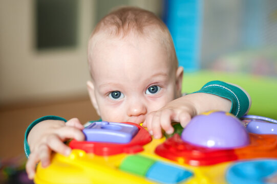 A young child leans over a bright toy, pressing buttons and exploring different sounds and lights. The playroom is filled with soft colors, and it's daytime