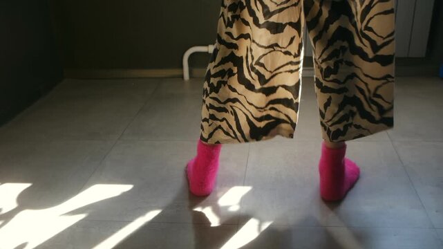 Woman wearing pink socks and zebra print pajama bottoms dancing on the floor at home, her feet moving rhythmically and joyfully in the morning sunlight casting beautiful shadows
