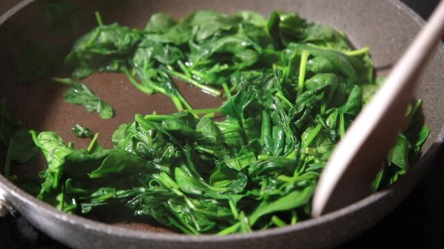 Close-up of fresh baby spinach leaves wilting and saut&eacute;ing in a hot skillet pan