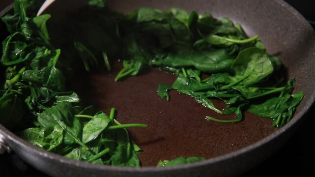 Close-up of fresh baby spinach leaves wilting and saut&eacute;ing in a hot skillet pan