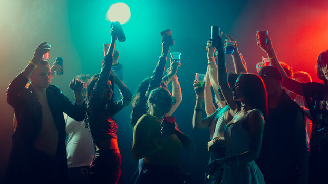 Group of diverse people partying, raising cups, colorful lights. Concept of nightlife party, youth, summer, festivity, celebration