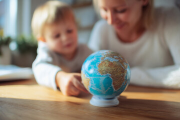Fototapeta premium Mother and baby looking at globe placed on desk while planning imaginary travel, medium close-up composition, bright cozy home environment, natural daylight