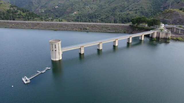 Aerial view of a water reservoir dam with an intake tower and concrete bridge in a green valley